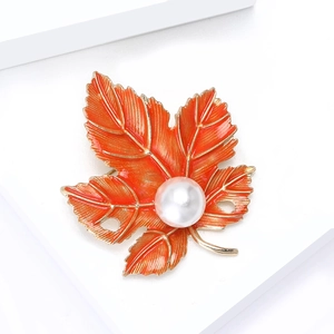 Elegant maple leaf brooch with red enamel and central pearl on a white geometric stand