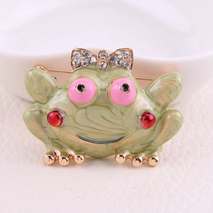 Detailed close-up of a green frog brooch featuring a pink rhinestone bow and enamel finish