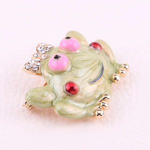 Detailed close-up of a frog brooch with green enamel, red gems, and clear rhinestones