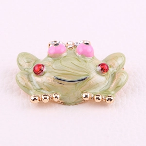 Detail of frog brooch with green enamel, red gemstone, and gold bow with rhinestones