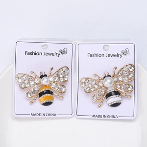Détail de broches abeilles dorées avec strass et perles élégantes sur céramique blanche