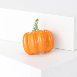 Vibrant orange pumpkin enamel brooch with green leaf detail on a white platform