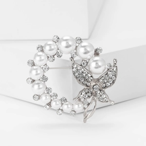 Detail einer runden Brosche mit weißen Perlen und Strass-Schmetterling auf weißer Stütze