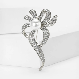 Détail macro de la broche ruban en strass avec une grande perle blanche centrale