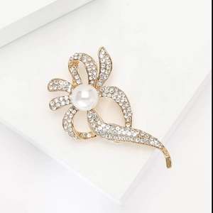 Détail de la broche fleur dorée avec perle blanche et strass sur un présentoir blanc