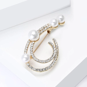Detail of minimalist gold hollow brooch with white pearls and sparkling rhinestones