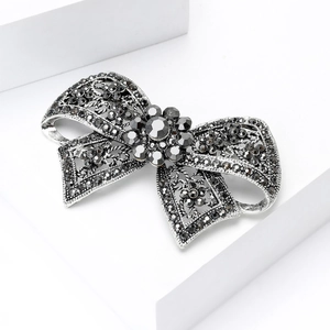 Elegant gun black vintage bow brooch with dark grey rhinestones on a white pedestal