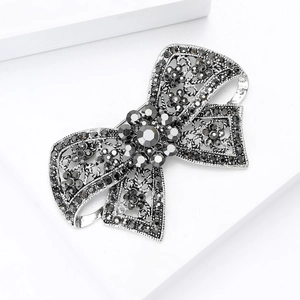Vintage gunmetal bow brooch with grey rhinestones on a white geometric platform