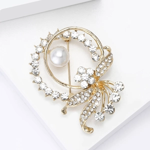 Elegant gold flower brooch with white rhinestones and a large pearl on a white pedestal