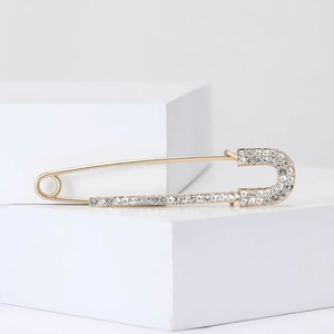 Squisita spilla da balia dorata con strass scintillanti su cubi bianchi minimalisti