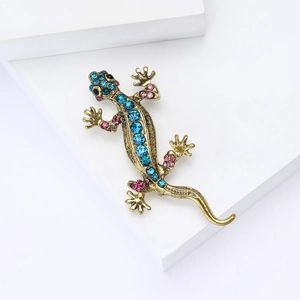 Spilla a lucertola dorata esagerata con strass blu e rosa su un piedistallo bianco