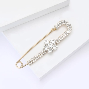 Détail d'une broche épingle dorée avec des fleurs en cristal sur présentoir blanc