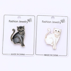 Detail view of black and white enamel cat brooches with bow accents on display card
