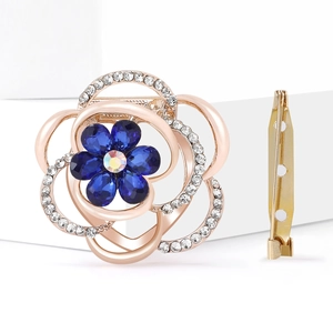 Floral brooch with blue gemstones and rose gold petals on a white geometric platform
