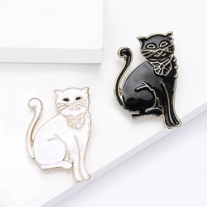Elegant black and white enamel cat brooches with gold edges on white geometric display stand
