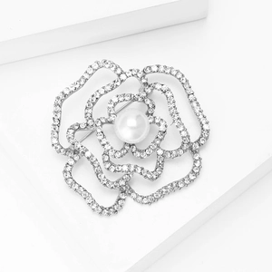 Dettaglio della spilla camelia con petali di strass e perla su un piedistallo bianco