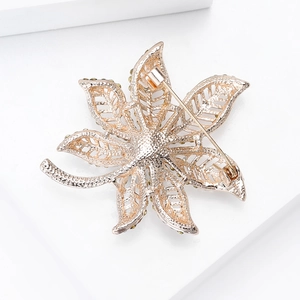 Elegant gold maple leaf brooch with crystal accents and textured petals on a white stand