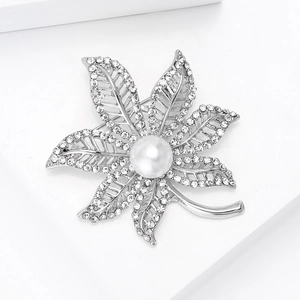Macro detail of a silver maple leaf brooch featuring a central pearl and inlaid rhinestones