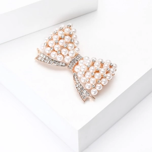 Élégante broche nœud en alliage doré avec perles blanches et strass sur un socle blanc