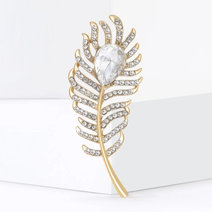 Exquisite gold feather brooch with sparkling white crystals on white geometric display stand