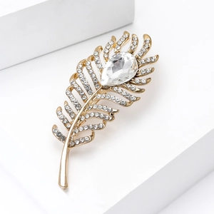 Detail of elegant gold feather brooch with crystals and teardrop gemstone on white