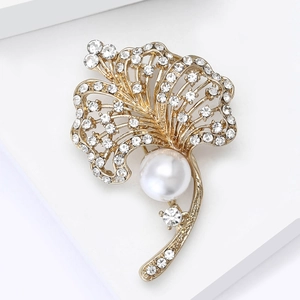 Detailed close-up of a golden leaf brooch featuring sparkling rhinestones and a white pearl