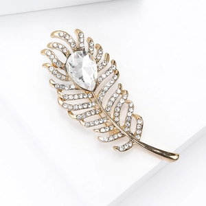 Detailed close-up of a luxury gold feather brooch with crystals on a white platform