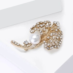 Close-up of golden leaf brooch with white pearl and sparkling crystals on white stand