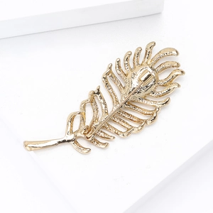 Exquisite gold feather brooch with intricate textures and rhinestones on a white display