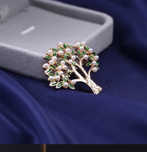 Detailed close-up of golden tree brooch with green enamel leaves and white pearls