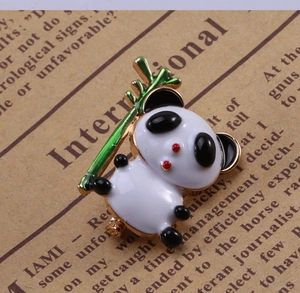 Gros plan d'une broche panda en émail tenant un bambou vert avec détails dorés