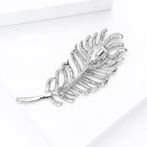 Macro shot of silver feather brooch showing detailed texture and pin closure mechanism