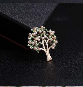 Detail of tree of life brooch with white pearls and green enamel on black leather box