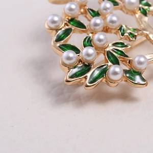 Macro view of vintage gold tree brooch featuring green enamel leaves and white pearls