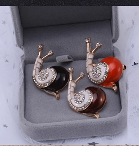 Detailansicht von drei Schnecken-Emaille-Broschen mit Strass auf einem grauen Samttablett