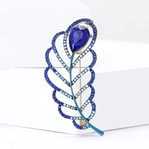 Detailed close-up of blue crystal feather brooch with gold base and pear-cut stone
