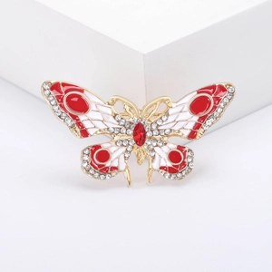 Détail d'une broche papillon en émail rouge et blanc sertie de strass brillants sur métal