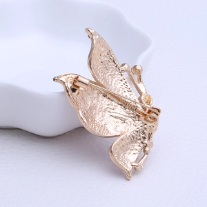 Elegant gold butterfly brooch with vintage metal texture on white ceramic display plate