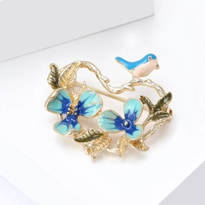 Detail view of blue enamel bird and flowers on a golden brooch with green leaves