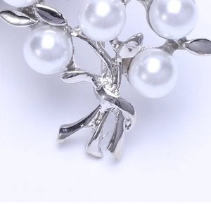 Macro shot of silver pearl brooch showing detailed metal leaves and smooth pearls