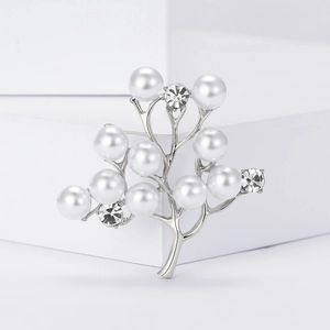 Broche arbre argentée élégante avec perles blanches et strass sur un socle blanc