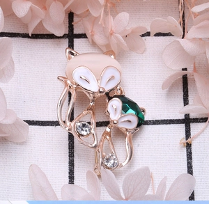 Detailed view of fox brooch with cat eye stone, emerald crystal and white enamel