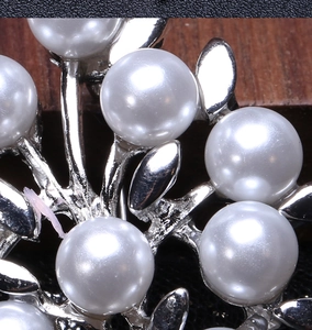 Macro detail of elegant silver-tone branch brooch with polished pearls on wood
