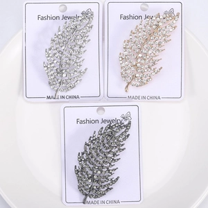 Detailed macro view of three crystal leaf brooches in silver, gold, and grey metal finish