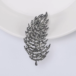 Macro shot of an elegant dark grey feather brooch with crystals on a white ceramic dish