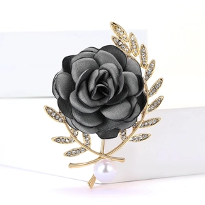 Vue détaillée d'une broche rose en tissu noir avec feuilles dorées et une perle