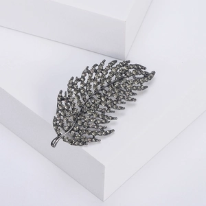 Detailed macro view of an elegant hollow leaf brooch with sparkling crystals on grey metal