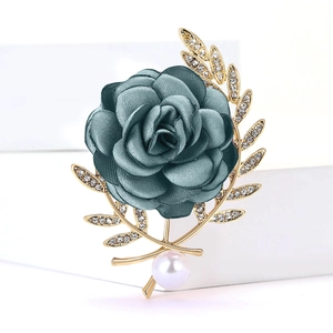 Détail de la broche fleur en tissu sarcelle avec feuilles dorées, strass et perle blanche