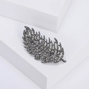 Detailed view of leaf brooch with gray rhinestones on elegant tiered white pedestals