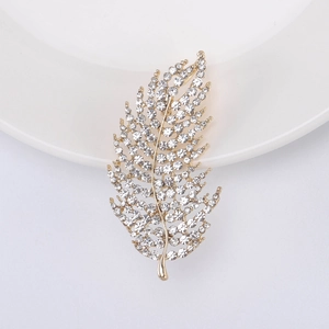Detailed close-up of a sparkling gold feather brooch with white zircons on a ceramic dish